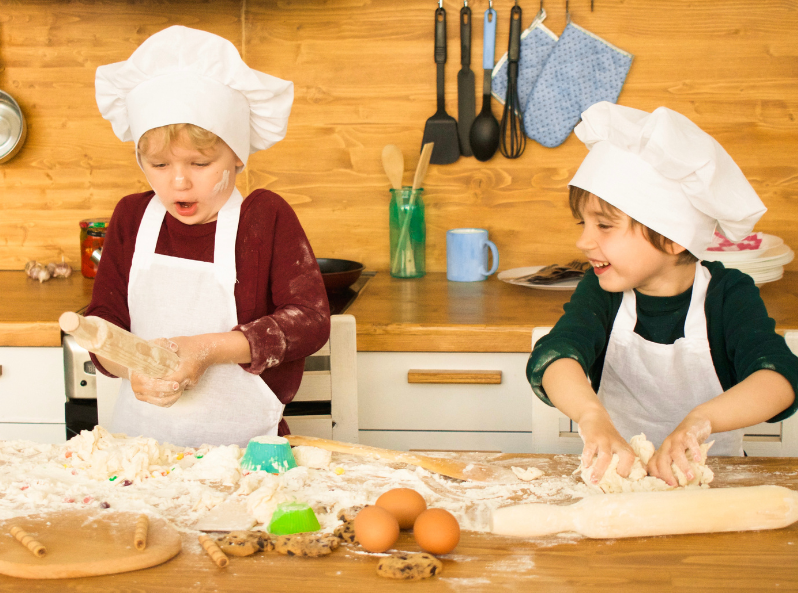 Dwoje dzieci wspólnie ugniata i wałkuje ciasto na drewnianym blacie kuchennym